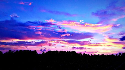 Low angle view of silhouette trees against dramatic sky