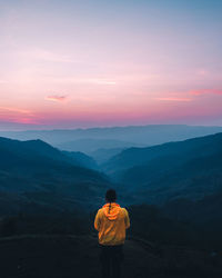 Rear view of man standing on mountain against orange sky