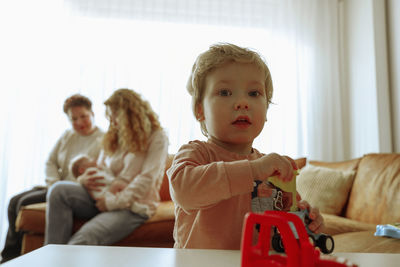Portrait of boy playing with toy with mother and grandmother on background 