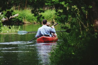 Rear view of people rowing canoe on lake against trees