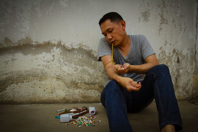 Man injecting syringe while sitting against wall