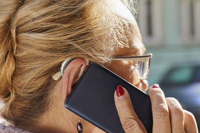 Close-up of senior woman with hearing aid using smartphone