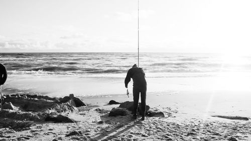 Silhouette man fishing at beach against sky