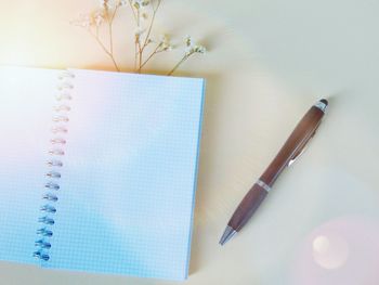 High angle view of pen and blank diary with flower on colored background