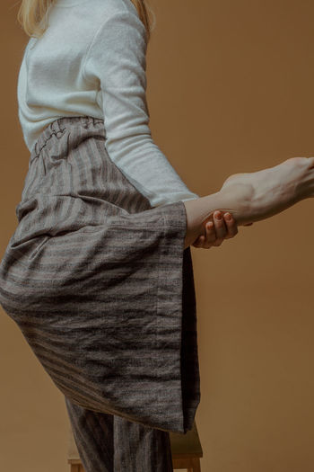 Midsection of woman standing on one leg against brown background