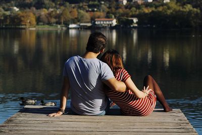 Rear view of couple sitting on pier over lake