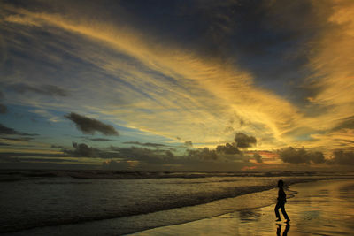 Silhouette boys play on the parangtritis beach alone at dusk with dramatic sunset sky.