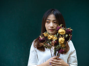 Young woman holding flower bouquet standing against colored background