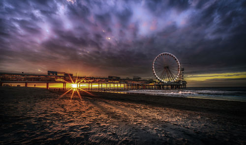 Illuminated ferris wheel at beach against sky at night