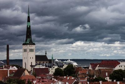 Church and buildings in city against cloudy sky