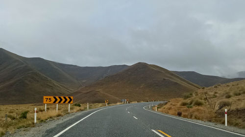 Empty road by mountains against sky