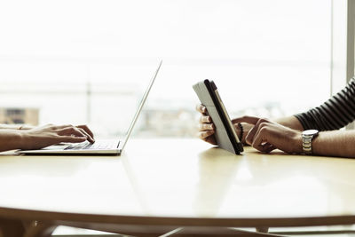 Cropped hands of university students using technologies at table in library