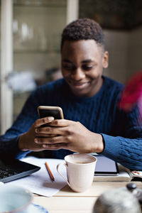 Smiling teenage boy using social media on smart phone while studying at home