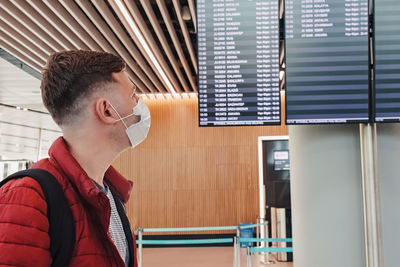 Man wearing a mask protection at an airport. looking to the screen with departure information. 