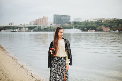 Portrait of young woman standing against river