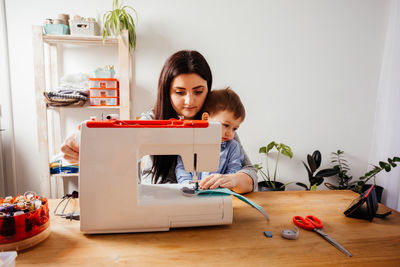 Mother with kid using sewing machine at home