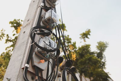 Low angle view of electric lamp hanging against sky