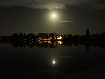 Silhouette trees by lake against sky at night