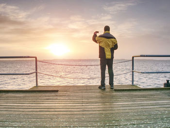 Rear view of man standing on railing against sea