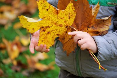 Close-up of hand holding yellow autumn leaf on field