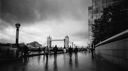 People walking in city against cloudy sky