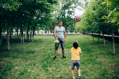 Full length of father and son playing on grass against trees