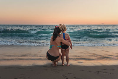 Friends on shore at beach against sky during sunset