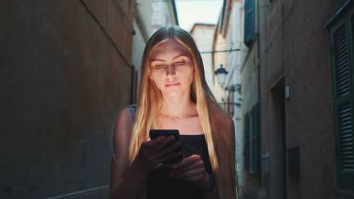 Young woman using mobile phone while standing on wall