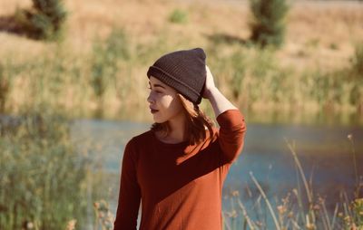 Young woman wearing knit hat standing against lake