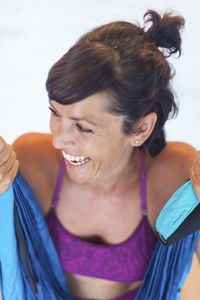 From above happy female laughing and looking away while sitting on ribbon during aerial yoga lesson in studio