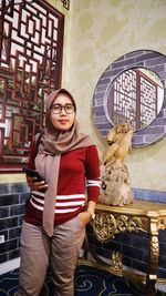 Portrait of smiling young woman standing against wall