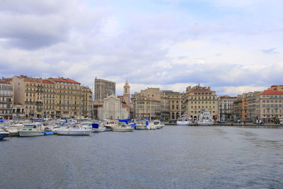 Sailboats moored on sea by buildings in city against sky