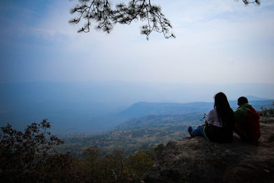 Rear view of people sitting on mountain against sky