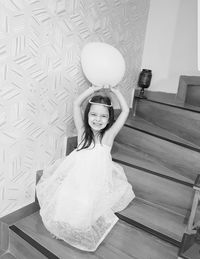 Portrait of girl holding balloon while sitting on steps at home