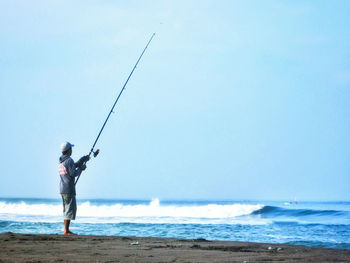 Man fishing at beach against sky