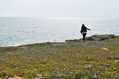 Woman standing in green field against sea and clear sky