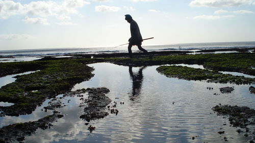 Side view of fisherman walking at beach against sky