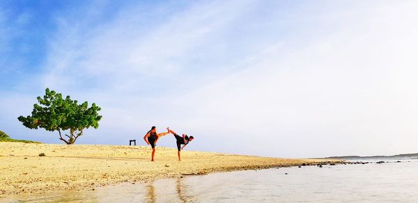 People doing exercising on beach against sky