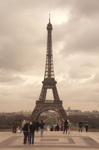 People by eiffel tower against cloudy sky