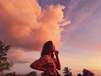 Woman standing on field against sky during sunset