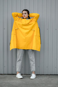 Girl in a yellow raincoat and gray jeans stands on a gray background. youth subculture