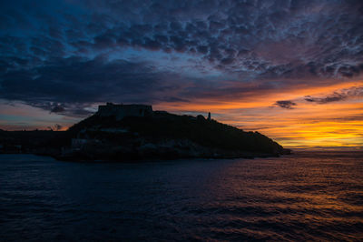 Scenic view of sea by buildings against sky at sunset