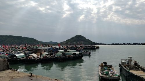 Boats moored at harbor by sea against sky