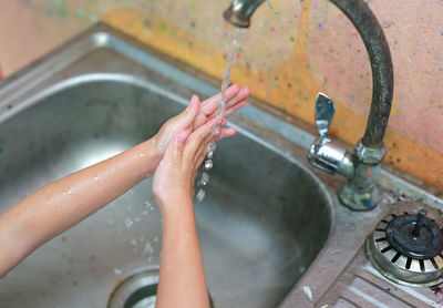 High angle view of woman drinking water from faucet in bathroom