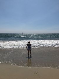 Rear view of woman standing on beach against clear sky