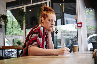 Woman with hand on chin writing on paper in cafe