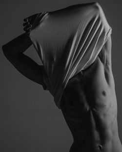 Midsection of shirtless man standing against black background