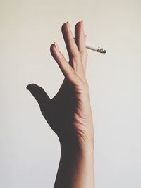 Cropped hand of woman holding cigarette over white background