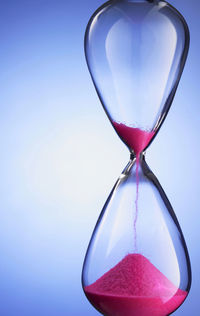 Close-up of hourglass with pink sand against blue background