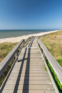 Boardwalk leading towards sea against clear sky